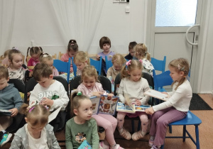 Dzieci siedzą w czytelni i oglądają książki