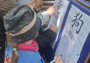 Dwoje dzieci z panią Anią rysują litery chińskie według wzoru