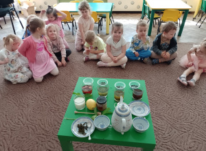 Dzieci siedzą na dywanie przy stoliku z herbatami