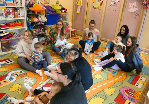 Mamy siedzą na dywanie i trzymają dzieci między nogami