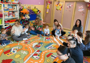 Mamy z dziećmi siedzą na dywanie i pokazują palce