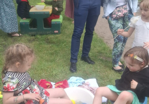 Dwie dziewczynki przenoszą stopami piłeczki z miski z wodą