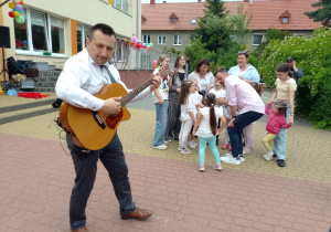 Pan Piotr gra na gitarze a grupa nauczycielek z dziećmi śpiewa