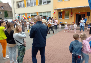Rodzice, dzieci i nauczycielki stoją w kole, a w środku stoi pan Piotr z gitarą