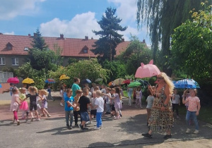 Dzieci z grupy Mrówki idą z parasolkami, a pozostałę tańczą w kółkach