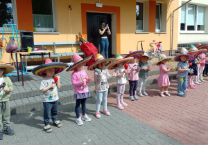 dzieci z grupy Motylki stoją w kapeluszach i grają na dzonkach i grzechotkach