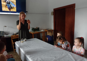 Pani opowiada dzieciom o pszczołach i pokazuje słoik z miodem