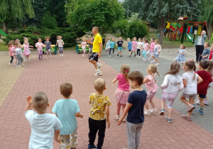 Dzieci stoją w kole podczas rozgrzewki prowadzonej przez trenera