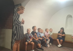 dzieci siedza w podziemiach zamku i słuchaja opowieści Pani kustosz
