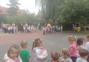 Dzieci w grupach stoją na placu przedszkolnym