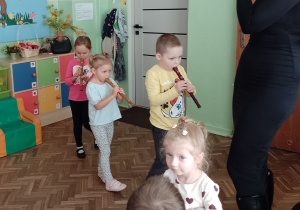 Troje dzieci i pani muzyk idą grając na flecie