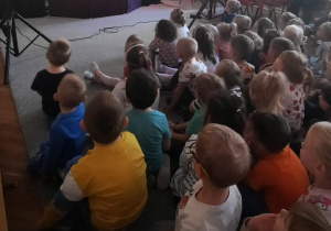 Dzieci siedząc na dywanie oglądają teatrzyk