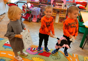 Dziewczynka trzyma obrazek z twarzą płaczącego chłopca, a dwoćh chłopców ciągnie maskotkę