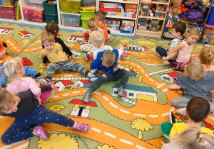 Dzieci w parach siedzą tylem do siebie trzymając się pod ręce i ćwiczą