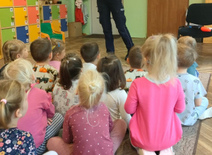 Pani policjantka stoi przed dziećmi, które siedzą na dywanie