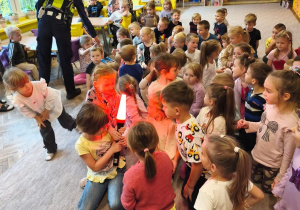 Pani policjantka podaje dzieciom sprzęt policyjny
