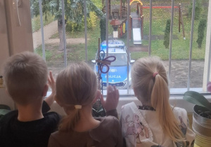 Troje dzieci przez okno patrzy na wóz policyjny