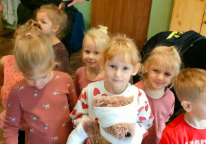 Strażak i kikoro dzieci stoją, a jedna dziewczynka trzyma zbandażowanego misia