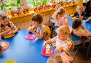 Dzieci siedzą przy stolikach i jedzą kanapki