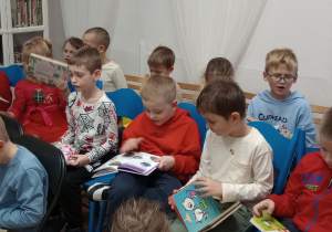 Dzieci siedzą na krzesłach i oglądają książki