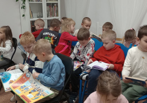 Dzieci siedzą na krzesłach i oglądają książki