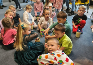 Dzieci siedzą na dywanie i trzymają słoiki z kapustą