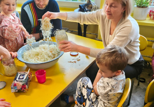 Dzieci z rodzicami przy stolikach ugniatają kapustę
