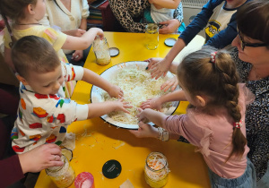 Dzieci z rodzicami przy stolikach ugniatają kapustę