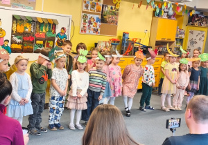 Dzieci w przepaskach z warzywami stoją podczas inscenizacji