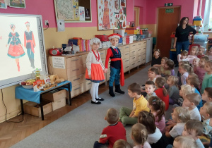 Dziewczynka z chłopcem w strojach kujawskich stoją przed dziećmi