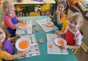 Cztery dziewczynki siedza przy stoliku i malują papierowe talerzyki