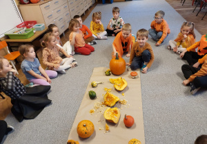 Dzieci siedzą na dywanie wokół dyń