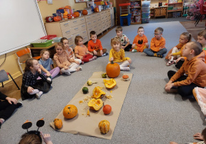 Dzieci siedzą na dywanie wokół dyń