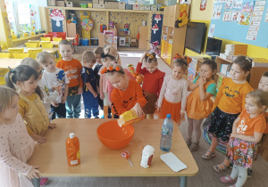 dziewczynka wsypuje mąkę do miski, a pozostałe dzieci stoją wokół stołu