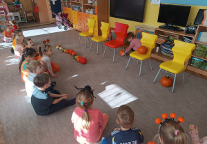 Dziewczynka układa dynie pod krzesłem, a inne dzieci obserwują