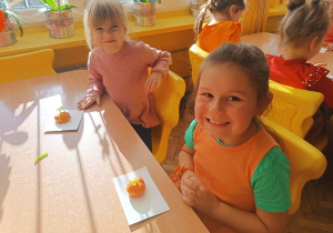 Dwie dziewczynki siedzą przy stole z ulepionymi dyniami