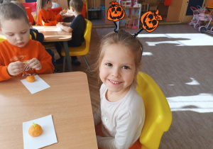 Dwoje dzieci siedzi przy stole z ulepionymi dyniami