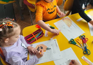 Dzieci przy stoliku wykonuja karty pracy z dyniami