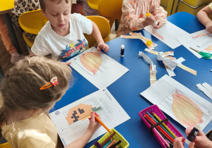 Dzieci przy stoliku wykonuja karty pracy z dyniami