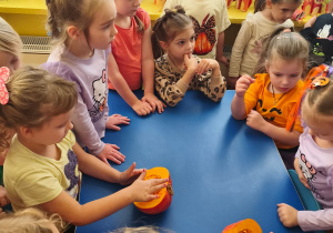 Dzieci stoją i siedzą przy stole, na którym leży przekrojona dynia