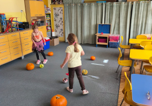 Dwoje dzieci toczy kijkiem piłkę między dyniami