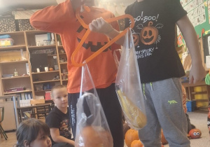 dwóch chłopców sprawdza ciężar dyń zawieszonych na wieszaku