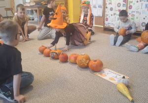 dziewczynka układa dynie, a pozostałe dzieci siedzą wokół