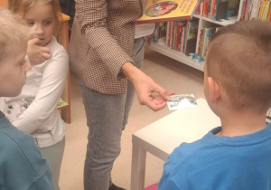Pani bibliotekarka podaje chłopcu kartę bibblioteczną