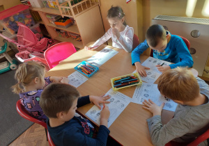 Pięcioro dzieci przy stoliku uzupełnia zadanie na karcie pracy
