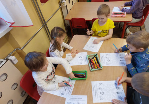 Kilkoro dzieci przy stoliku uzupełnia zadanie na karcie pracy