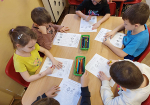 Kilkoro dzieci przy stoliku uzupełnia zadanie na karcie pracy