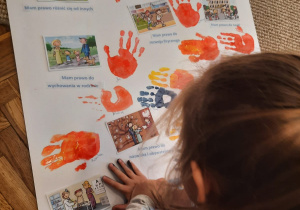 Dziewczynka robi odcisk dłoni na plakacie z prawami dziecka