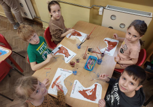 Piecioro dzieci przy stoliku maluje sylwetę niedźwiadka