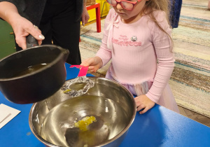 Dziewczynka trzyma klucz nad miską podczas lania wosku